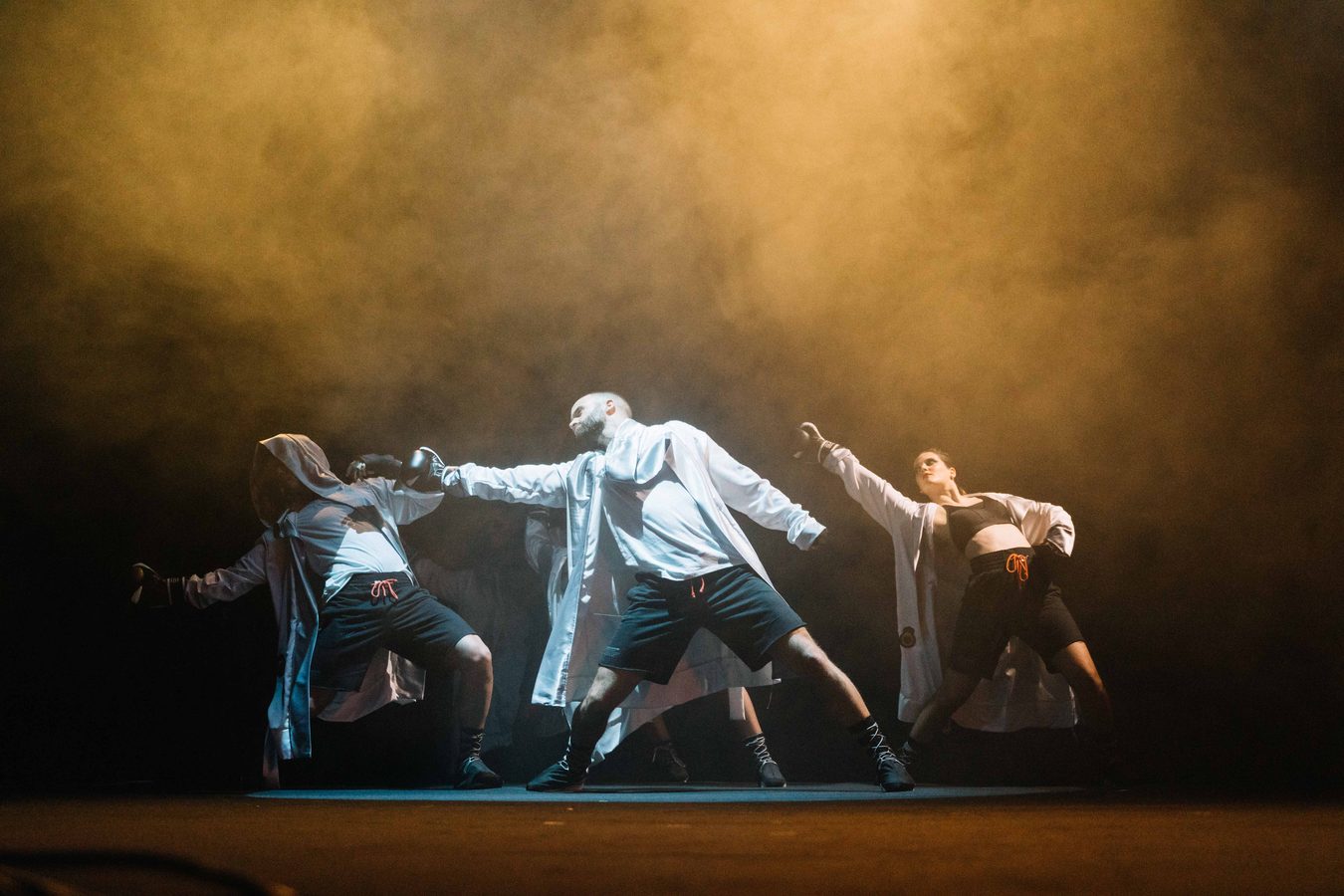 Quatro bailarinos em palco, em contraluz e fumo