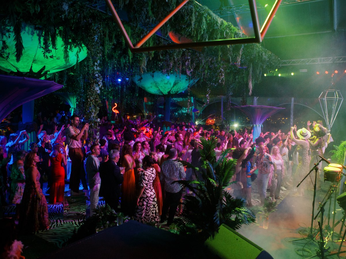 Pista cheia de convidados sob uma estrutura iluminada a verde, ao ar livre, no evento WILD