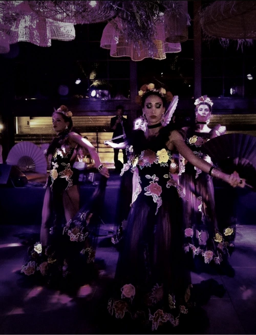 Performers com leques e figurinos florais sob luz violeta